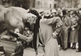Black-and-white photo of Charlotte Despard speaking at an anti-fascist rally in at Trafalgar Square in London, c 1930s. She is kneeling
            forward with her left arm and her waist and her right arm hooked forward in a fist.