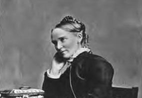 Low resolution black and white three-quarter-length photo of Frances Ridley Havergal sitting on a chair, Her hair is braided in a crown on top of her head. She is wearing a dark, long-skirted dress and jacket with white at the throat and wrists. She sits at a table with two drawers, with a basket like a jewel box on the table and a fat book in her lap. Underneath the image her signature is reproduced: "Frances R. Havergal".