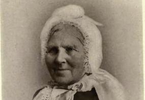 Black and white photograph of Catharine Parr Traill, wearing a white cap tied under her chin. Her strong features are clearly visible, but detail around the image is blurry and fades to nothing. Her signature is reproduced below.