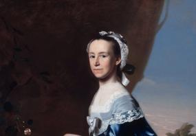 Painting of Mercy Otis Warren by John Singleton Copley. She stands in an outdoor background of trees and flowers, holding one hand out, and wearing a deep blue gown with quantities of lace at the wrists, frills and more lace elsewhere, and a silver bow in the centre of the bodice. She has a lacy white cap tied with a silver ribbon on her brown hair.